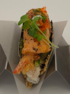 sushi rice, crab meat, deep fried shrimp, salmon, cream cheese, avocado, lemon, cucumber, sweet sauce, creamy sauce, torched, green onion, kaiware Gancho Taco