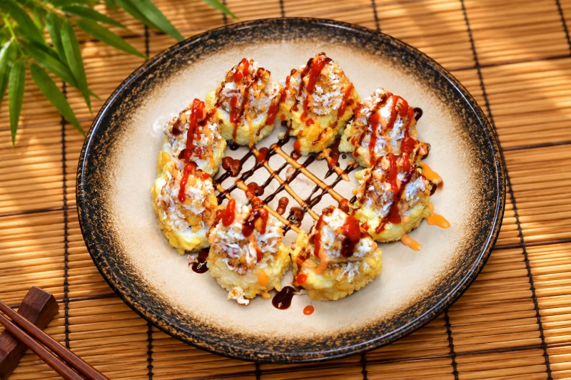 Hot. Deep-fried spicy tuna roll topped with crab salad, crunch, crispy onion, sriracha, spicy mayo, unagi sauce, and green onion. R27_Mt. Rainier Roll - Deep-Fried Roll